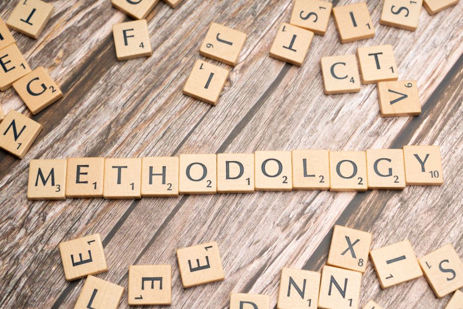 Wooden letter tiles spelling 'methodology' on a textured wooden surface, emphasizing research.